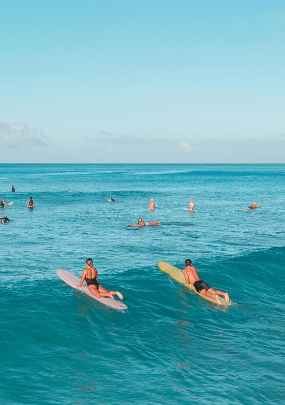 Surfers paddling out at a sunny Bali surf retreat beach