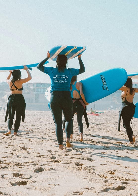 Women carrying surfboards across the beach at a Byron Bay surf retreat